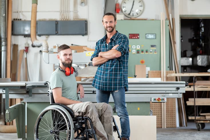 Dwóch uśmiechniętych pracowników, jeden z nich na wózku inwalidzkim